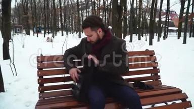 在冬天的公园里，一个长胡子的人坐在草地上。 商人打开箱子拿书